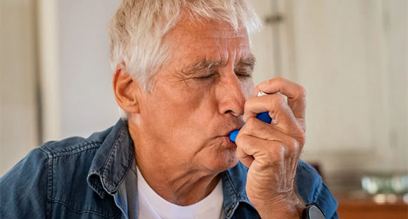 an older man using an inhaler to help manage his asthma  