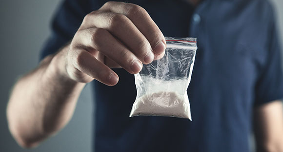 an ominous picture of a man holing a plastic bag of cocaine powder