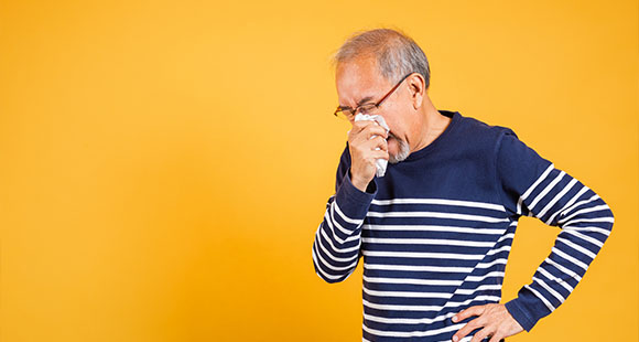 an older man blowing his nose with a tissue on a yellow background