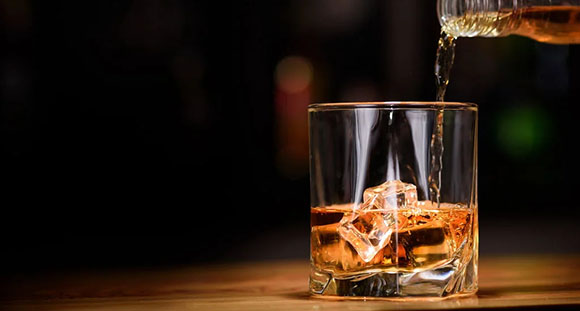 a glass on a wooden surface being filled with whiskey