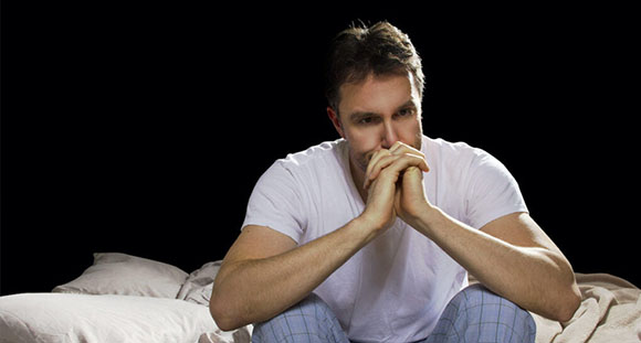 a man sitting contemplatively on a bed in the darkness