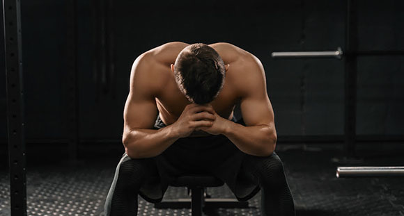 a shirtless muscular man with his hands to his face in the middle of a dark gym