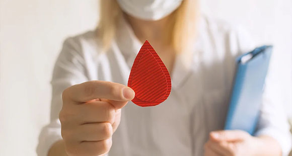 a woman holding a red corrugated cardboard in the shape of a blood drop