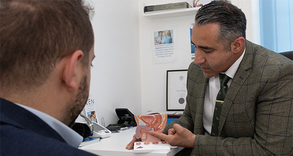 Mr. Almashan in a consultation with a patient, pointing at the diagram of a pelvis