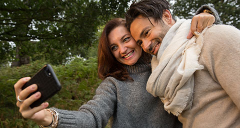 a smiling couple posing for a selfie in the woods 