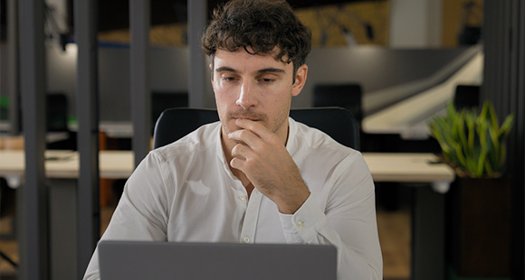 a young man sitting in an office performing research on a laptop