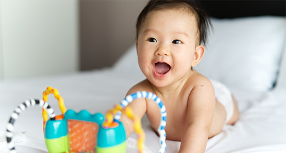 a happy baby laying on a bed with a toy