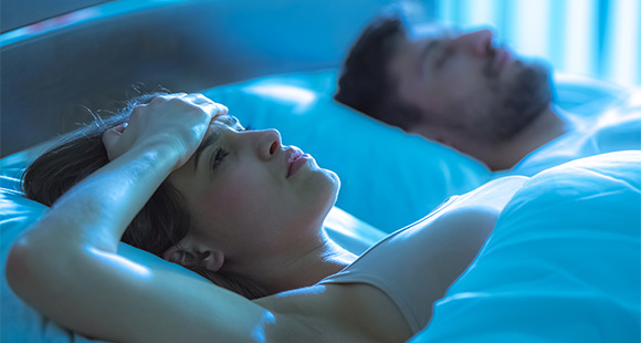 a woman laying awake in bed with a man next to her sleeping soundly