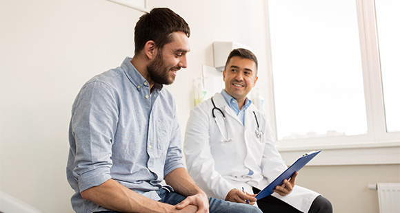 a doctor holding a clipboard and sitting next to a male patient conversing with him
