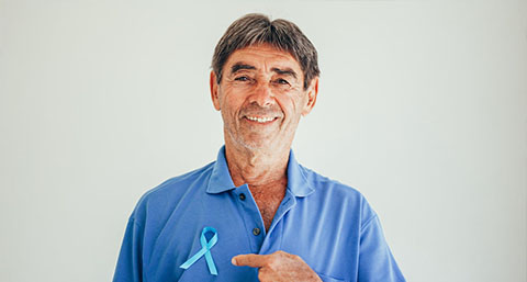a doctor smiling and pointing at the prostate cancer ribbon pinned to his shirt