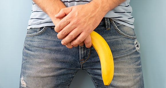 a man with his arms crossed against his groin holding a banana